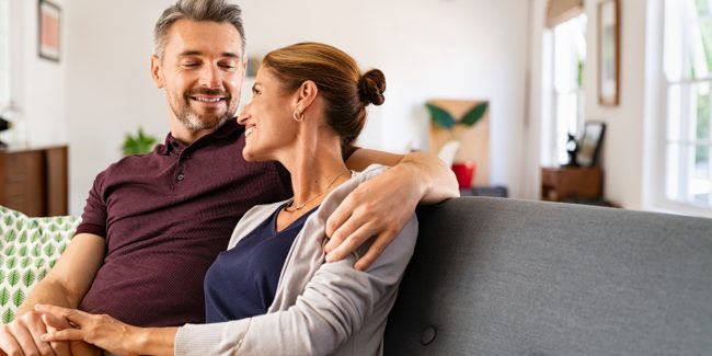 Smiling middle-aged couple sitting at a white table, using a laptop and holding a credit card, planning a purchase or managing finances together.